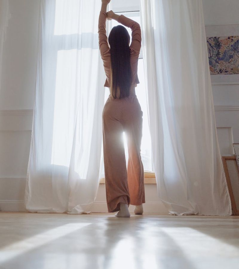 Person doing a gentle morning stretch by a large window with sunlight streaming in.